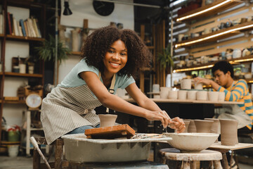 Creative afro American young woman artist molding clay on pottery wheel, Workshop in ceramic studio, clay making of a ceramic pot on the pottery wheel, hobby and leisure with pleasure concept