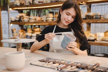 Beautiful young woman holding pottery instrument for scraping, smoothing, shaping and sculpting. Lady siting on bench with pottery wheel and making clay pot