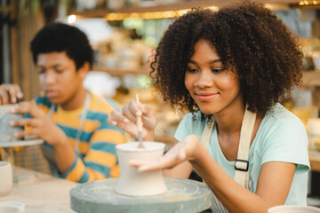 Creative afro American young woman artist molding clay on pottery wheel, Workshop in ceramic studio, clay making of a ceramic pot on the pottery wheel, hobby and leisure with pleasure concept