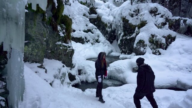 A couple of people take a selfie in the snow by a stream on an Alaska trail during winter
