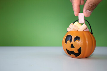 The hand puts a candy on the smiling pumpkin head, pumpkin party for children. Halloween, front view with green and white background. jack o lantern