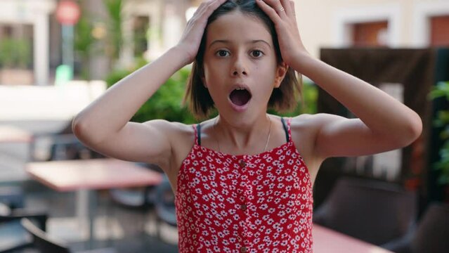 Adorable hispanic girl standing with surprise expression at street