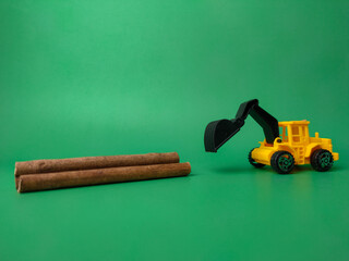 Excavator with wooden stick on green background. Conceptual image of illegal logging.