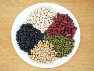 Five type of natural grains consisted of soybeans, black beans, red beans, white beans , and green beans on white the dish. Top view photo, blurred.