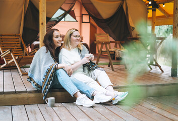 Obraz na płótnie Canvas Two young women friends drinking tea and relaxing in glamping in the woods