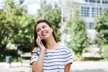 Portrait of young woman student with long hair using mobile phone in city park