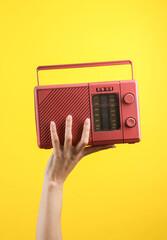 Female hand holding a pink retro radio receiver on a yellow background