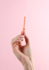Woman's hand holding birthday candle on pink background