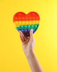 Woman's hand holding pop it antistress sensory device. Yellow background
