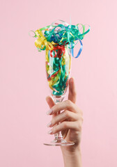 Woman's hand holds glass with streamer on a pink background. Party concept