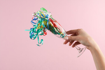 Woman's hand holds glass with streamer on a pink background. Party concept