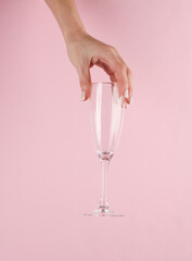 Empty champagne glass in a female hand on a pink background