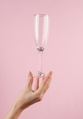 Empty champagne glass in a female hand on a pink background