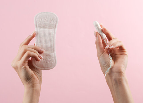 Woman's hand holds a tampon and pads on pink background. Feminine hygiene, menstruation, critical days