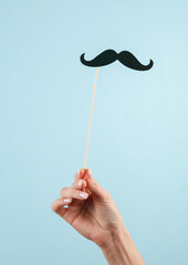 Male mustache on a stick for a photo booth in a female hand on a blue background