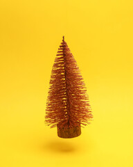 Miniature Christmas tree floating in the air on a yellow background with a shadow. Creative idea. Minimal concept. Levitating objects