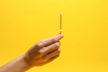 Hand holding birthday candle on yellow background