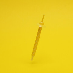 Yellow birthday candle levitating on a yellow background