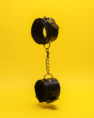 Leather bdsm handcuffs levitating on yellow background. Dominance. Sex games. - obrazy, fototapety, plakaty