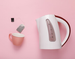 Plastic electric kettle with tea bag and cup on pink pastel background. Top view