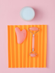 Massage jade roller for facial massage and gua sha with a jar of cream on a colored background....