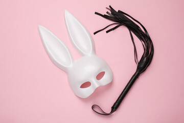 Sex shop toys. Rabbit mask with leather whip on a pink background