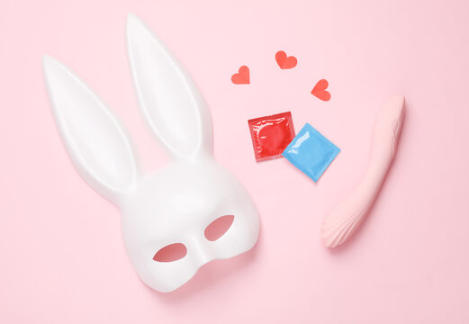 Sex games. Rabbit mask, vibrator, condoms and hearts on a pink background. Top view