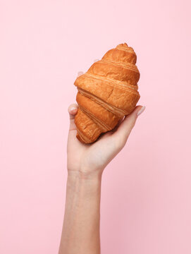 Female hand holding a croissant on a pink background