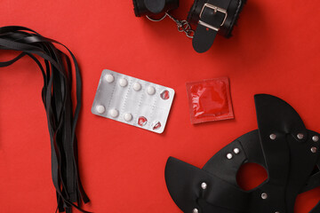 The concept of safe sex. Contraceptive pills and condom with sex shop toys on red background