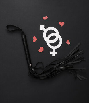 Leather whip from a sex shop, gender symbols with hearts on black background. Sex, love games