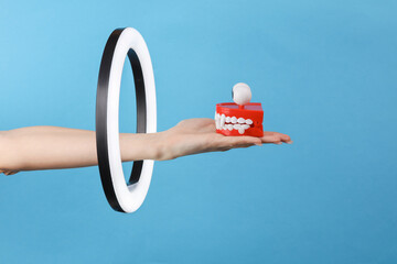 Woman's hand holds joke funny jamping jaw through led ring lamp on blue background. Creative idea.