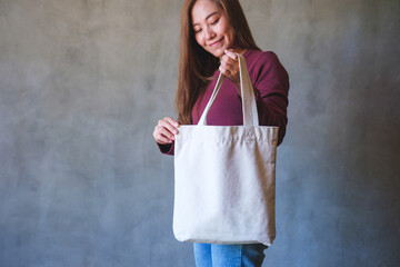 Portrait image of a young woman holding and carrying a white cloth bag for reusable and environment...