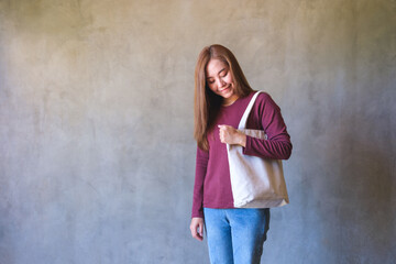 Obraz na płótnie Canvas Portrait image of a young woman holding and carrying a white cloth bag for reusable and environment concept