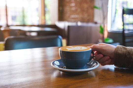 Closeup image of a hand holding coffee cup on wooden table