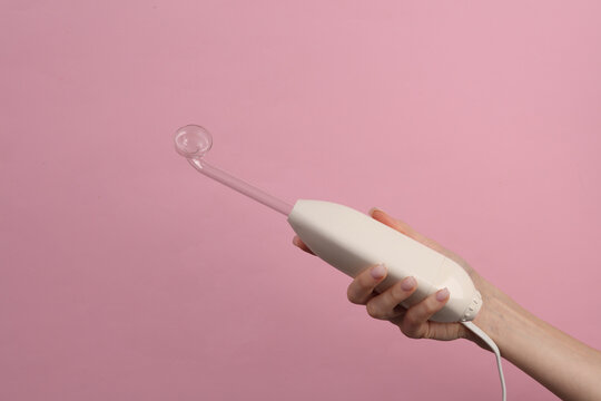 A woman's hand holds a device for local dorsenvalization on a pink background. Treatment of acne, skin diseases and alopecia