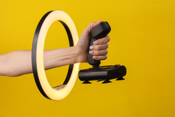 Woman's hand holds retro joystick through led ring lamp on yellow background. Creative idea.