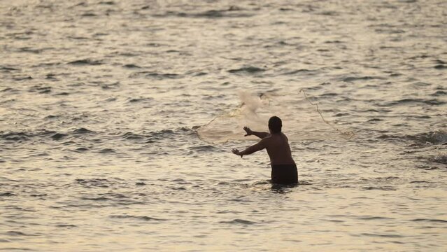 Local balinese fisherman throwing net in ocean to catch fish at sunset