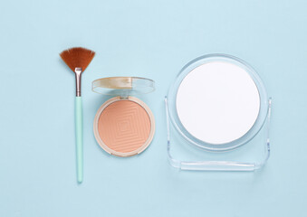 Makeup brushes with powder box and mirror on blue background