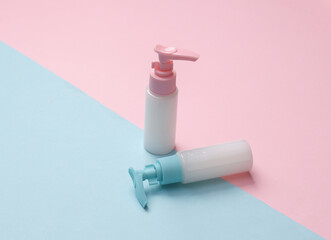 Bottles of cream or liquid soap with a dispenser on a blue-pink pastel background. Creative beauty still life