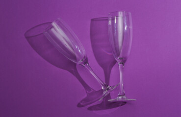 Aesthetic shot of empty champagne glasses with long shadow. Purple background