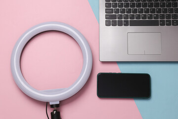 Led ring lamp with laptop and headphones on pink blue background. Gear for blogging and vlogging. Top view