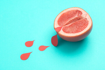 Menstruation concept, women's health. Ripe grapefruit half vagina symbol with blood drops on blue...