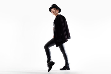 Stylish young woman in a black hat and jacket, posing on a white background in a photo studio