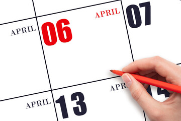 A hand holding a red pen and pointing on the calendar date April 6. Red calendar date, copy space,...