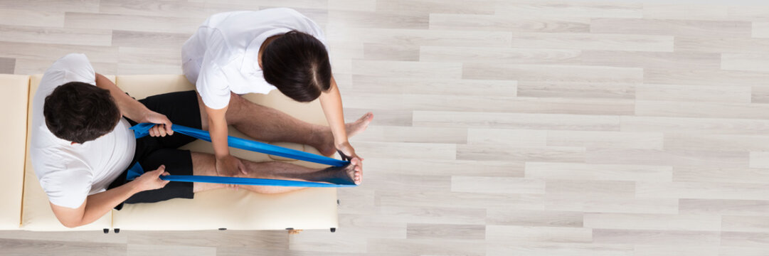 Female Therapist Assisting Patient While Exercising