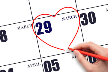 A woman's hand drawing a red heart shape on the calendar date of 29 March. Heart as a symbol of love.