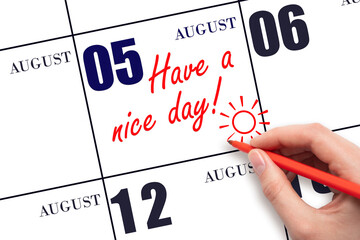 The hand writing the text Have a nice day and drawing the sun on the calendar date August 5
