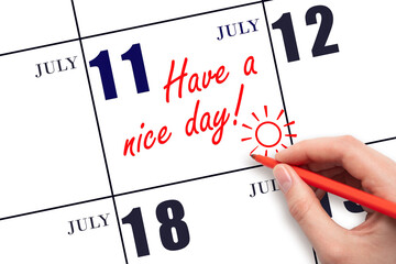 The hand writing the text Have a nice day and drawing the sun on the calendar date July 11