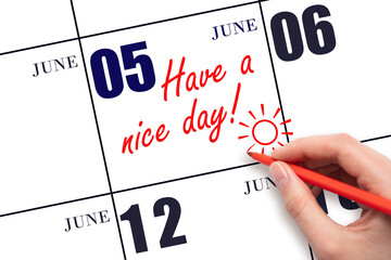 The hand writing the text Have a nice day and drawing the sun on the calendar date June 5