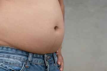 Closeup shot of asian man overweight stomach with jean trousers and cement blur background, planning exercise and loss weight for good health in the feature, healthcare and gym concept copy space